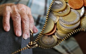 Eine alte Hand öffnet einen Reißverschluss hinter dem Euro-Münzen zu sehen sind