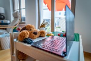 Ein Teddybär sitz vor einem Laptop und sieht aus als würde er arbeiten
