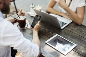 Zwei Personen sitzt an einem Tisch, die eine Person guckt auf sein Handy, die andere auf einen Laptop