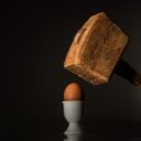 Ein Holzhammer, der kurz davor ist auf ein Ei zu schlagen