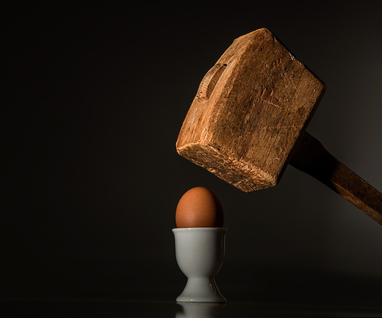 Ein Holzhammer, der kurz davor ist auf ein Ei zu schlagen